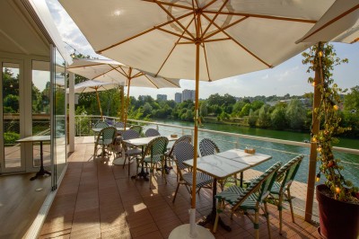 Miniature Location salle Lagny-sur-Marne (Seine-et-Marne) - Aux Deux Barrés #7 Terrasse extérieure avec bar en carrelage violet, tables, parasols et guirlandes lumineuses sous un ciel dégagé.