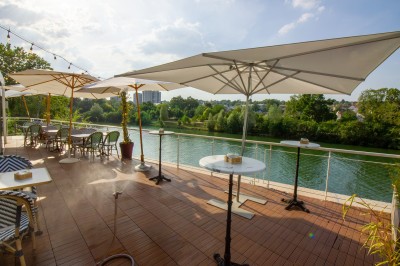 Miniature Location salle Lagny-sur-Marne (Seine-et-Marne) - Aux Deux Barrés #8 Terrasse extérieure avec bar en carrelage violet, tables, parasols et guirlandes lumineuses sous un ciel dégagé.