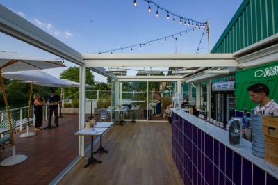 Miniature Location salle Lagny-sur-Marne (Seine-et-Marne) - Aux Deux Barrés #9 Terrasse extérieure avec bar en carrelage violet, tables, parasols et guirlandes lumineuses sous un ciel dégagé.