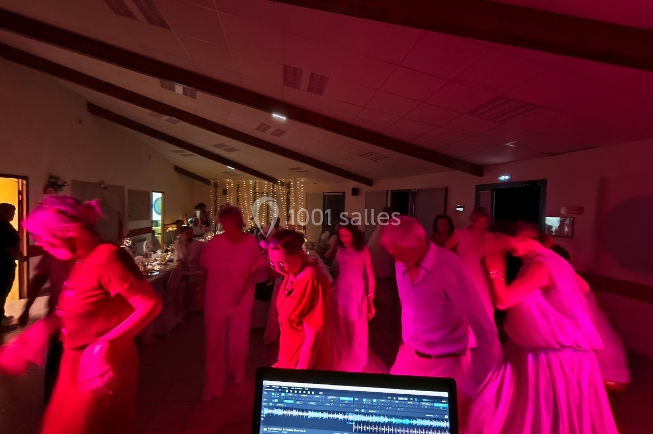 Des personnes dansent dans une salle éclairée par des lumières rouges, avec une table de mixage visible au premier plan.