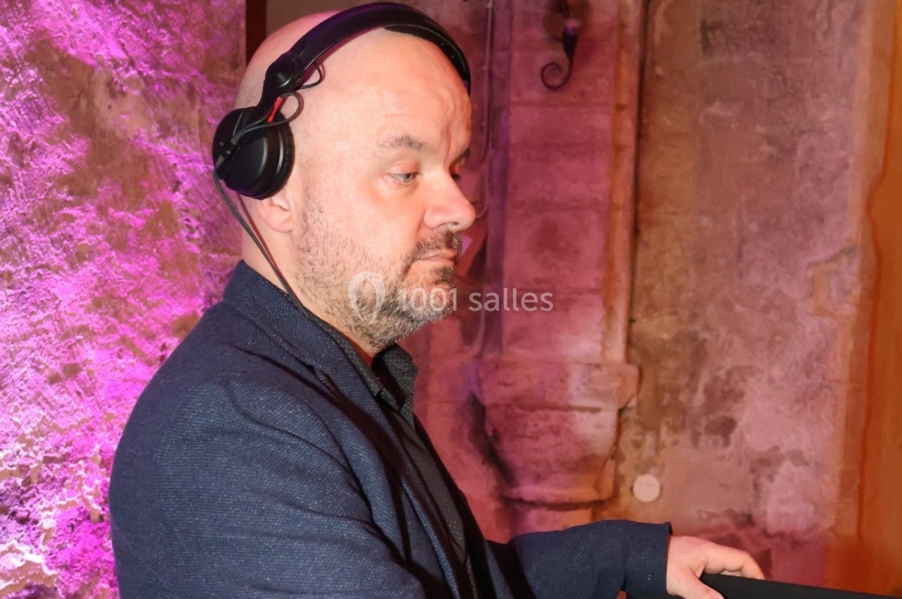 Un homme portant un casque audio se tient devant un mur en pierre éclairé par une lumière rose.