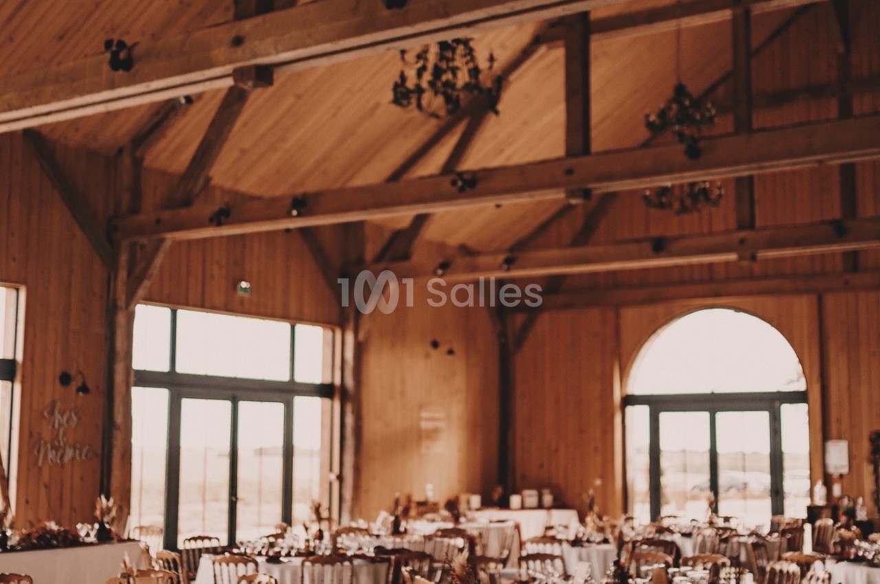 Salle de réception en bois avec charpente apparente, tables dressées et grandes baies vitrées.