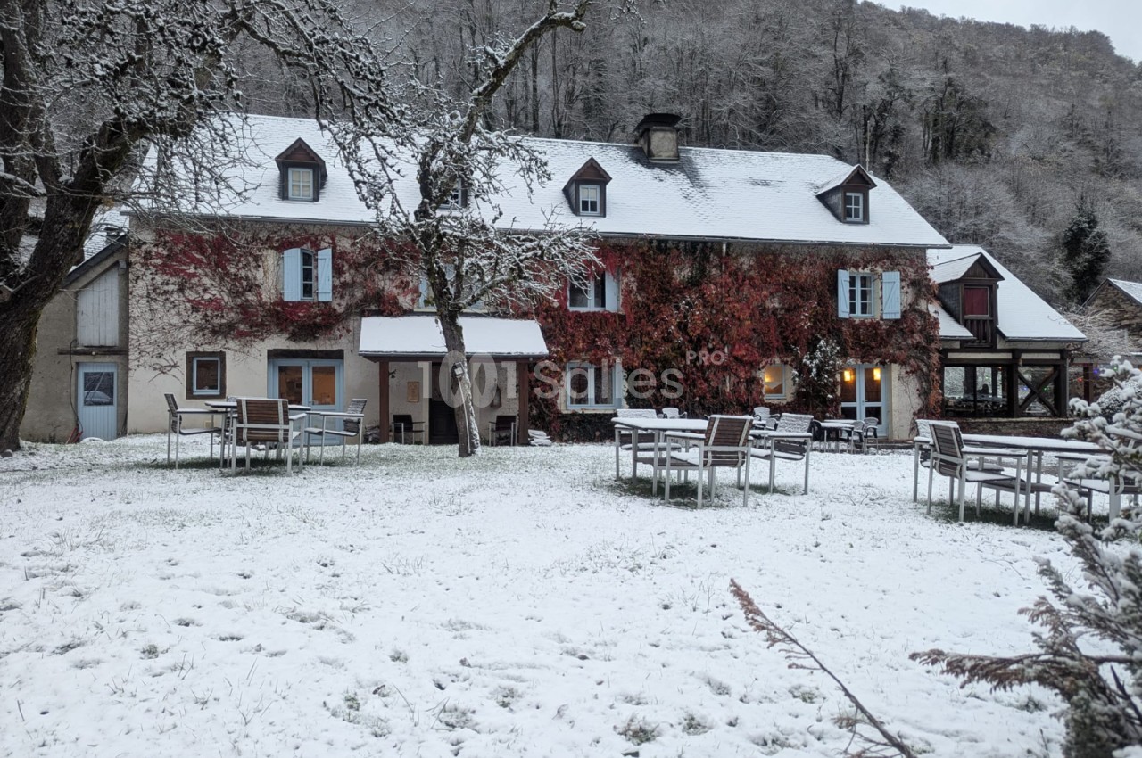 Bâtiment de pierre aux façades couvertes de vigne vierge rouge, sous une fine couche de neige, avec des tables et chaises de jardin disposées sur la pelouse enneigée.