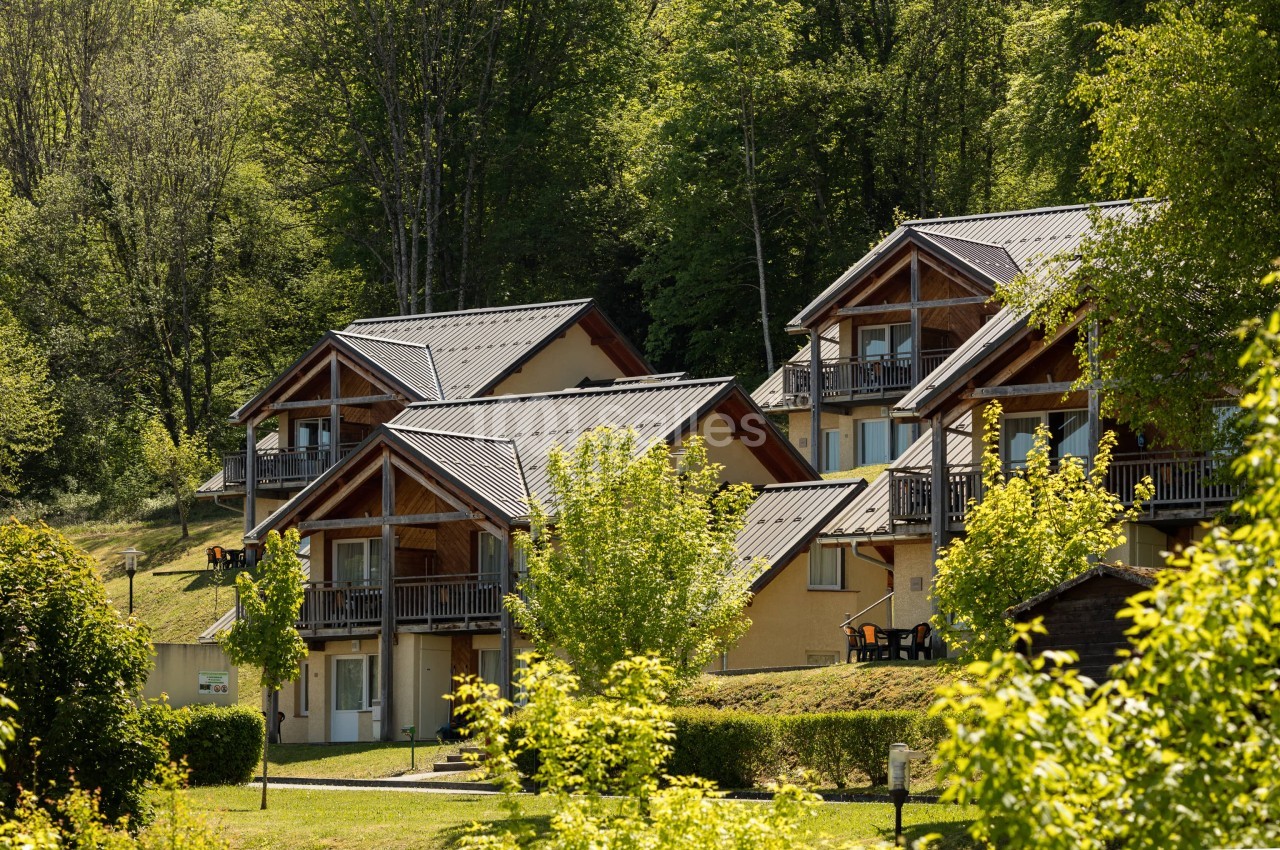 Ensemble de chalets en bois et façades beige clair aux toits métalliques, avec balcons, nichés en lisière de forêt verdoyante, en extérieur.