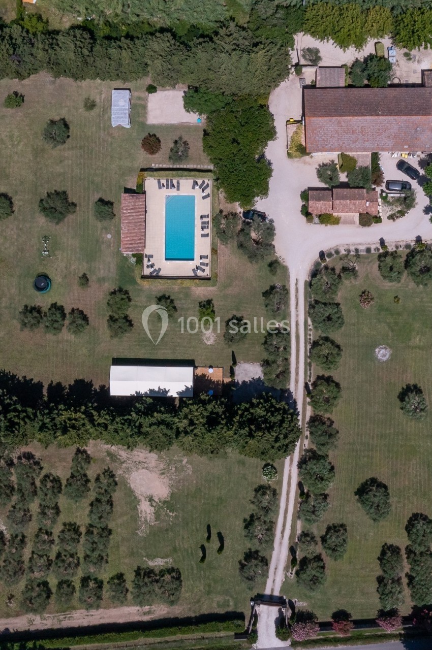 Vue aérienne d'une propriété avec piscine, jardin arboré, bâtiments en pierre et allées entourées de verdure.