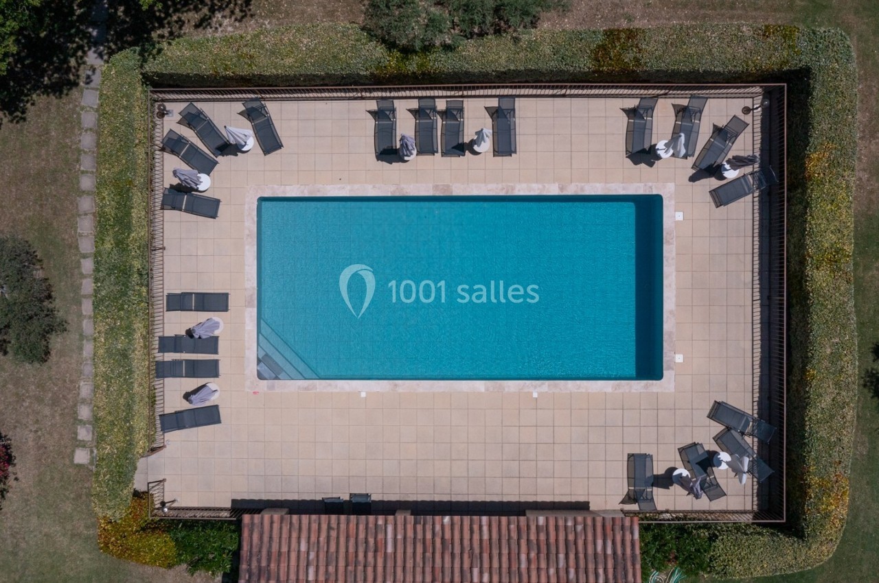 Vue aérienne d'une piscine rectangulaire entourée de chaises longues et de haies dans un espace extérieur aménagé.