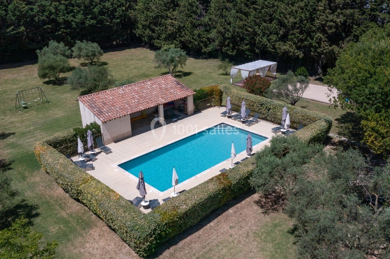 Vue aérienne d'une piscine rectangulaire entourée de haies, avec transats et parasols, dans un jardin arboré.