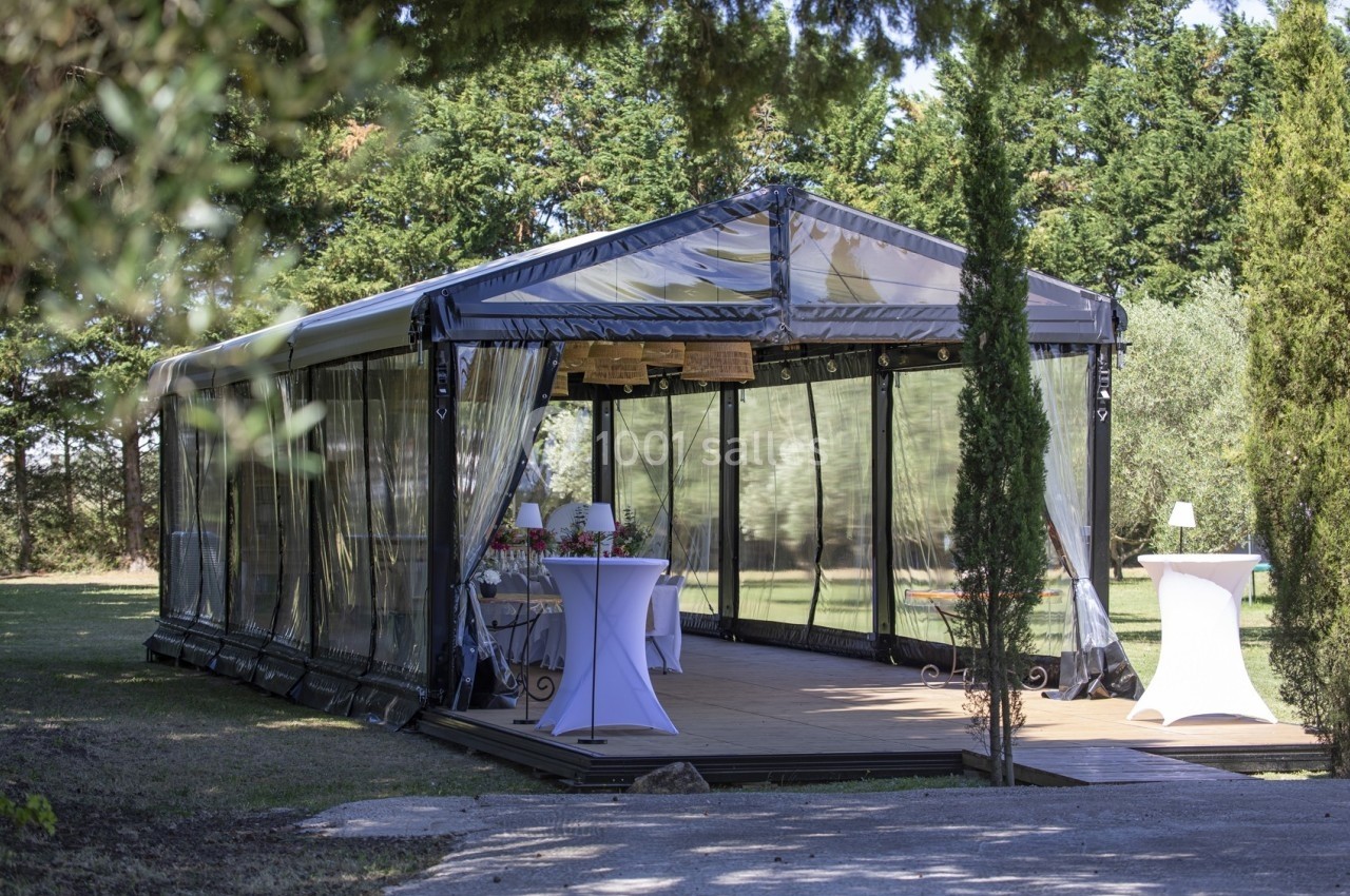 Tente transparente installée en extérieur, aménagée avec des tables hautes et des décorations pour un événement.