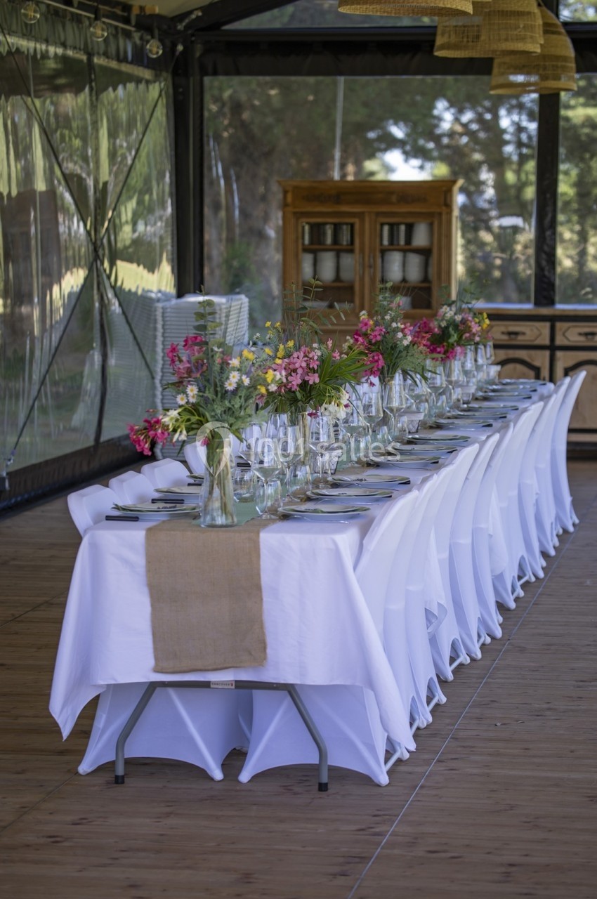 Table dressée avec nappes blanches, chemins de table en lin et bouquets de fleurs colorées dans une salle lumineuse.