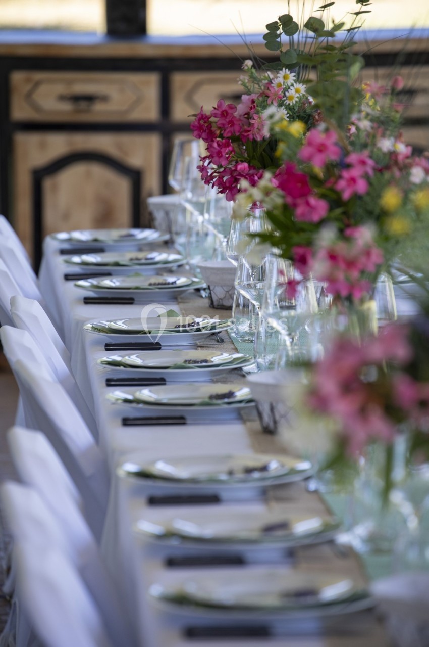 Table dressée avec nappes blanches, couverts alignés et bouquets de fleurs colorées en centre de table.