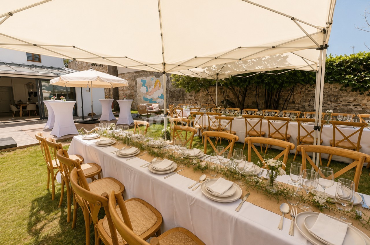 Terrasse aménagée pour banquet avec tables blanches dressées, chaises en bois, voiles de protection et murs en pierre.