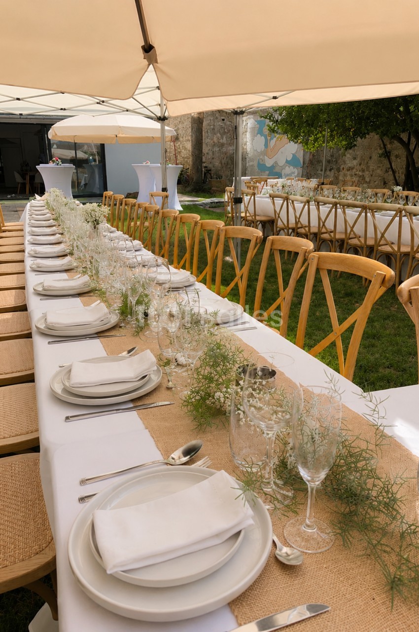 Salle dressée en extérieur avec table banquet blanche sous tentes beiges, chaises bois clair et décoration florale légère.