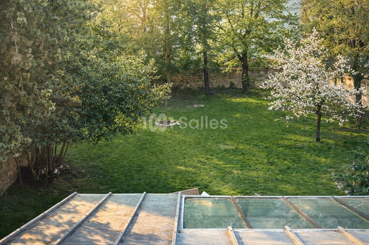 Jardin arboré avec pelouse verte, arbres fruitiers en fleur et structure vitrée au premier plan.
