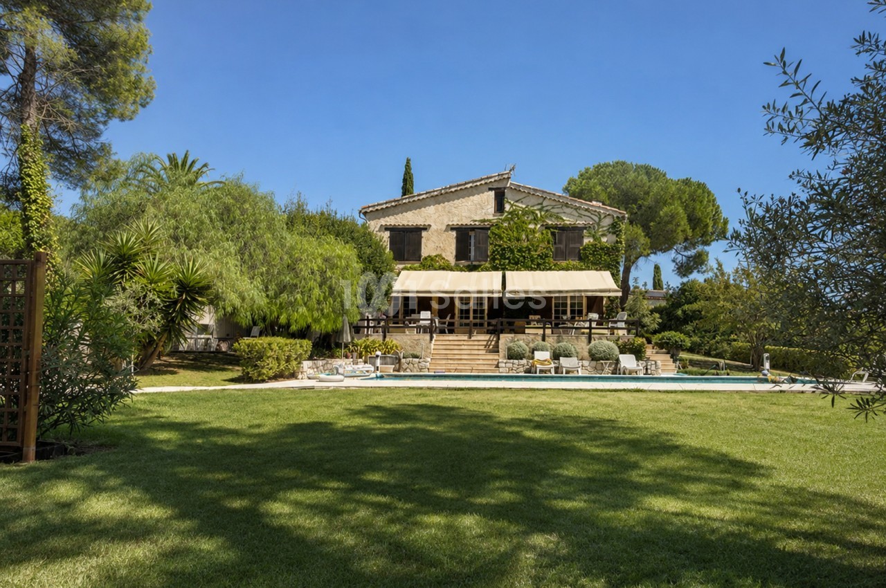 Maison de style provençal avec piscine, terrasse ombragée et jardin paysagé en premier plan.