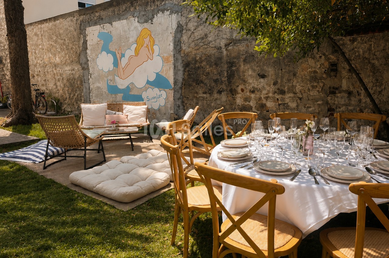 Jardin intérieur aménagé pour un repas - table dressée en nappe blanche, chaises en bois, zone lounge avec canapé et fresque murale.