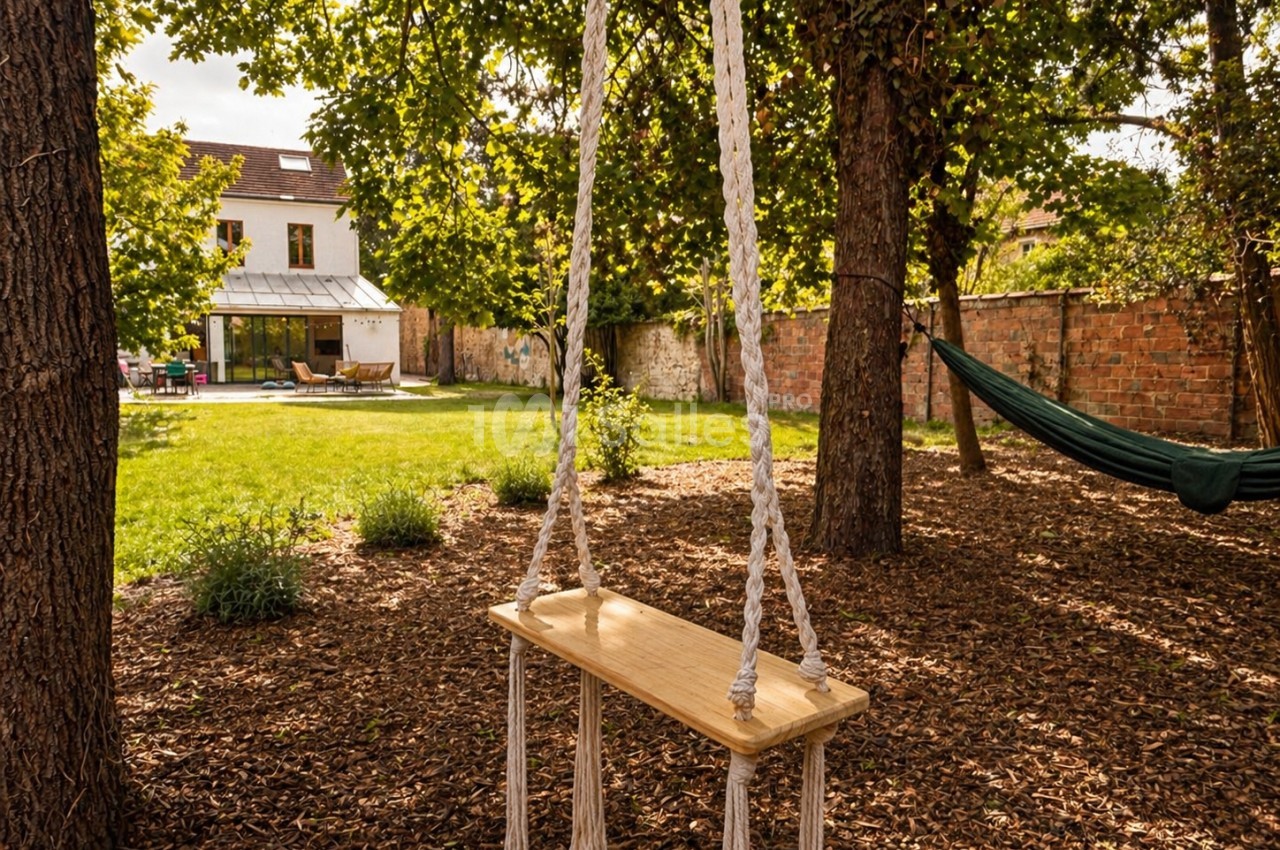 Jardin arboré avec balançoire en bois, hamac et maison contemporaine avec terrasse aménagée.