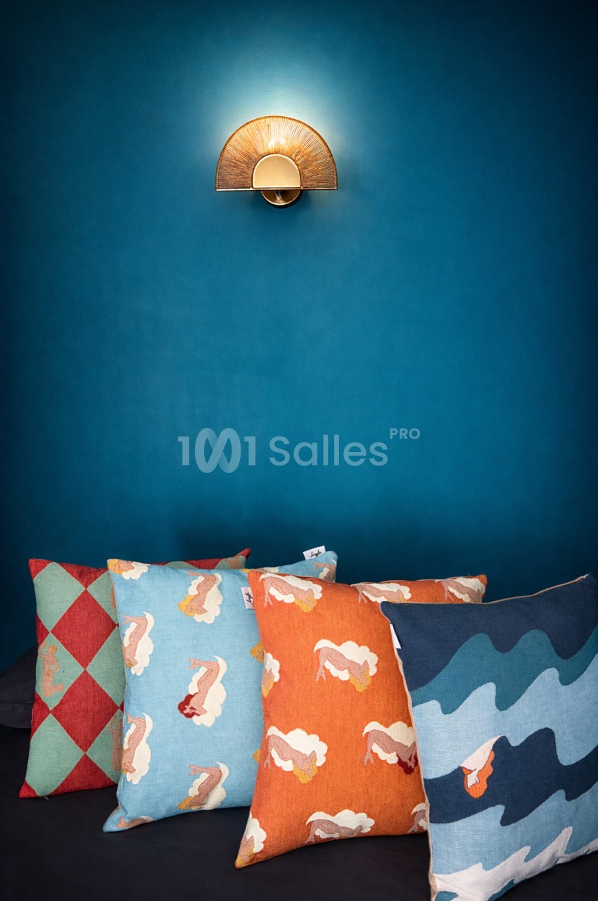Applique art-déco en laiton sur mur bleu avec coussins colorés en tissu motifs géométriques et nuages.