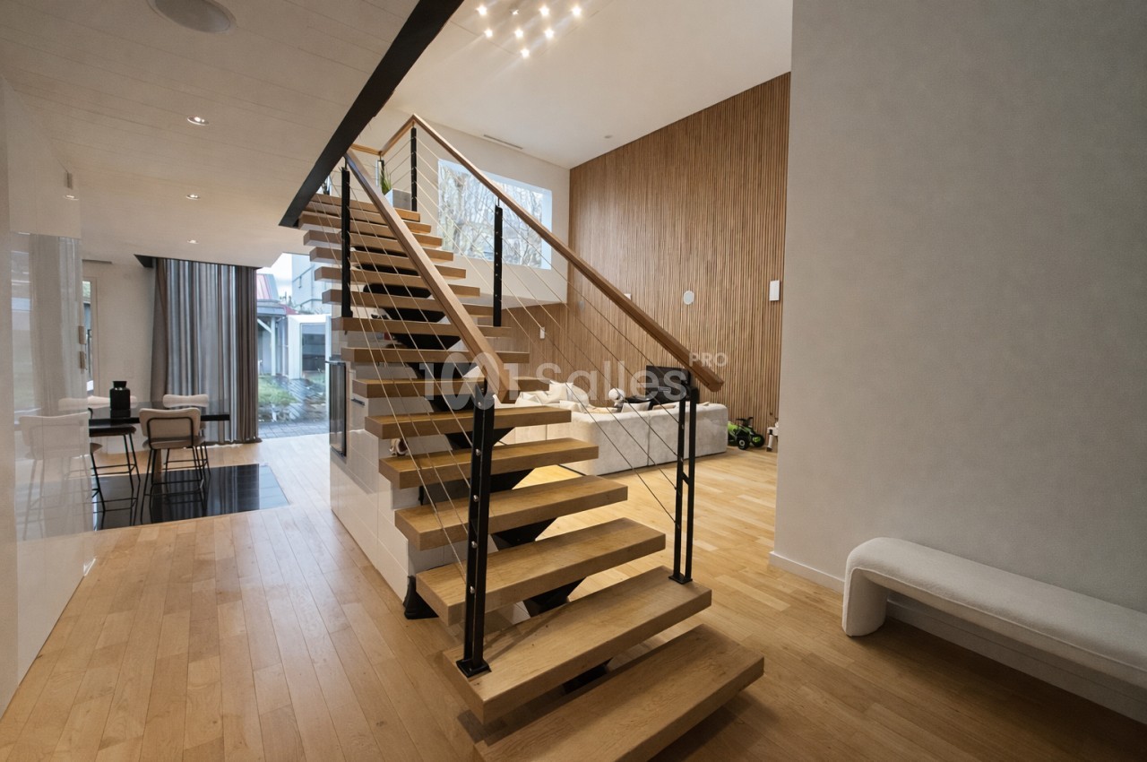 Intérieur contemporain avec escalier central en bois et rampe noire, parquet clair, mur en bois naturel et accès vers espace extérieur.
