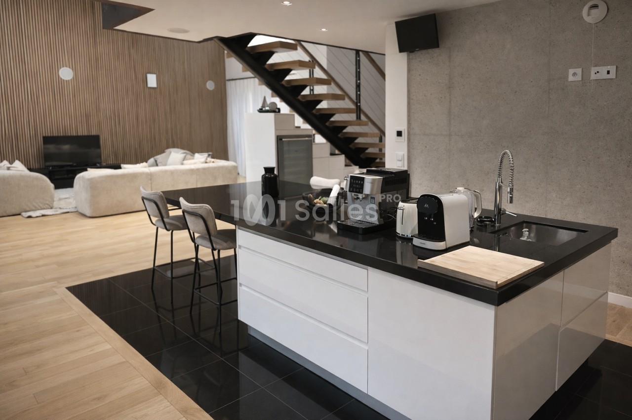 Espace de réception avec cuisine ouverte, escalier design et zone de repos avec canapés.