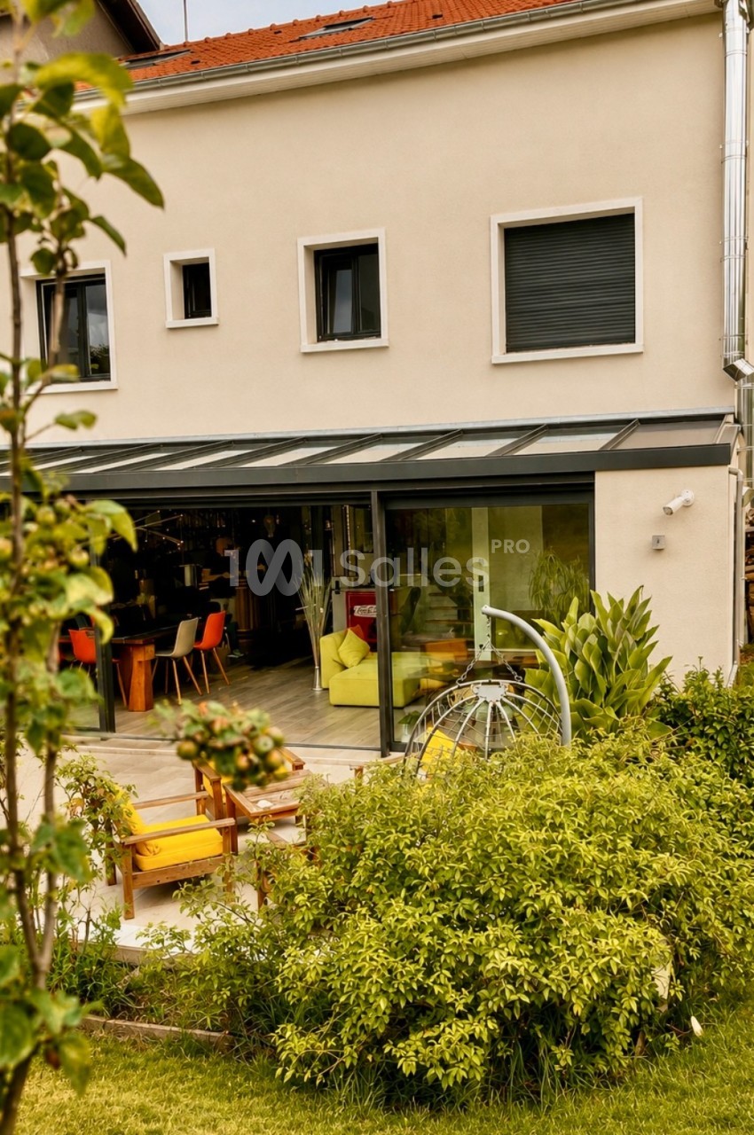 Maison jaune et crème avec terrasse couverte aménagée - chaises orange, canapé jaune, jardin verdoyant.