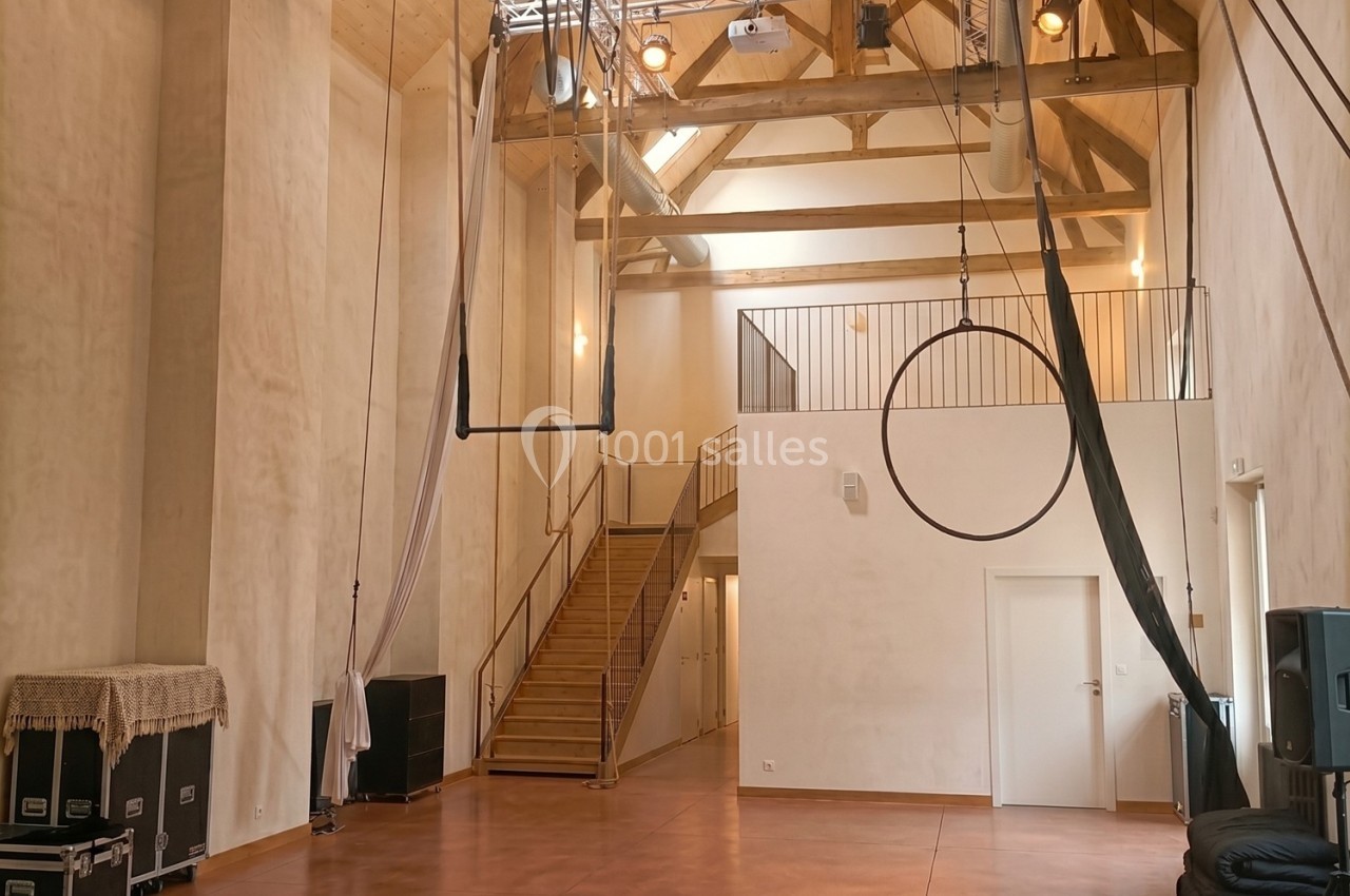Salle spacieuse avec structure en bois apparente, équipée pour des activités aériennes et artistiques.