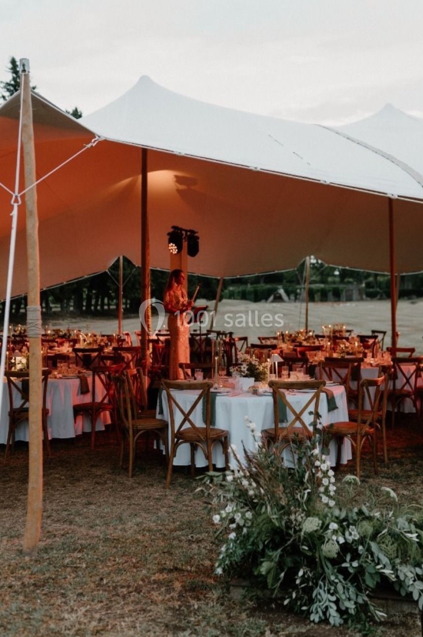 Dîner en plein air sous une tente blanche avec tables décorées et éclairage chaleureux au crépuscule.