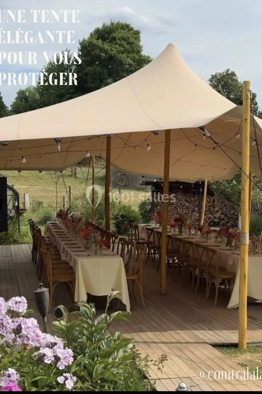 Tente beige installée sur une terrasse en bois, abritant des tables décorées pour un événement en extérieur.