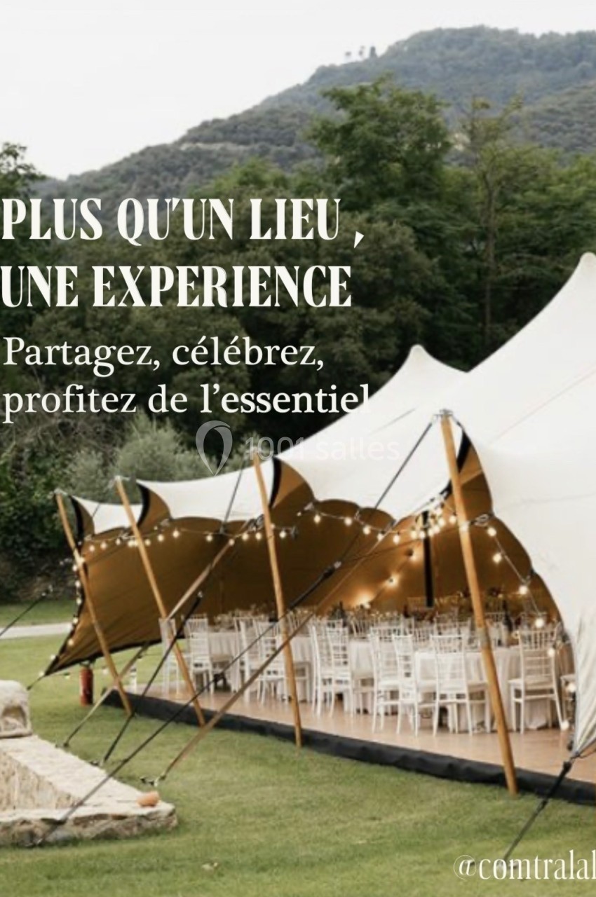Grande tente blanche installée en extérieur, entourée de verdure, avec des tables et chaises décorées pour un événement.