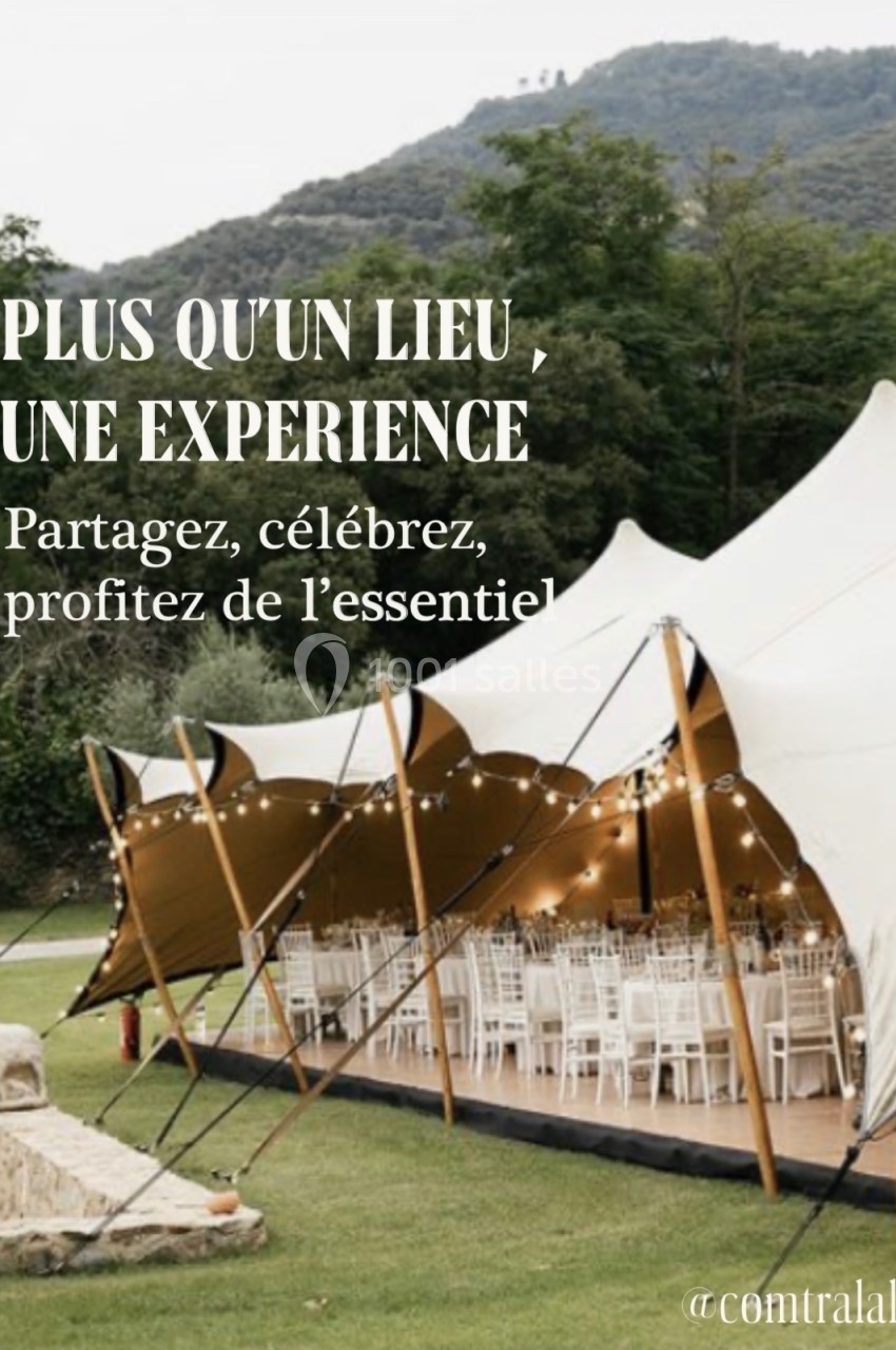 Tente élégante installée en extérieur avec tables dressées pour un événement, entourée de verdure et de collines.