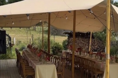Miniature Comtralala #2 Tables décorées pour un dîner en plein air sous une tente éclairée de guirlandes lumineuses, près d'un bâtiment en pierre.