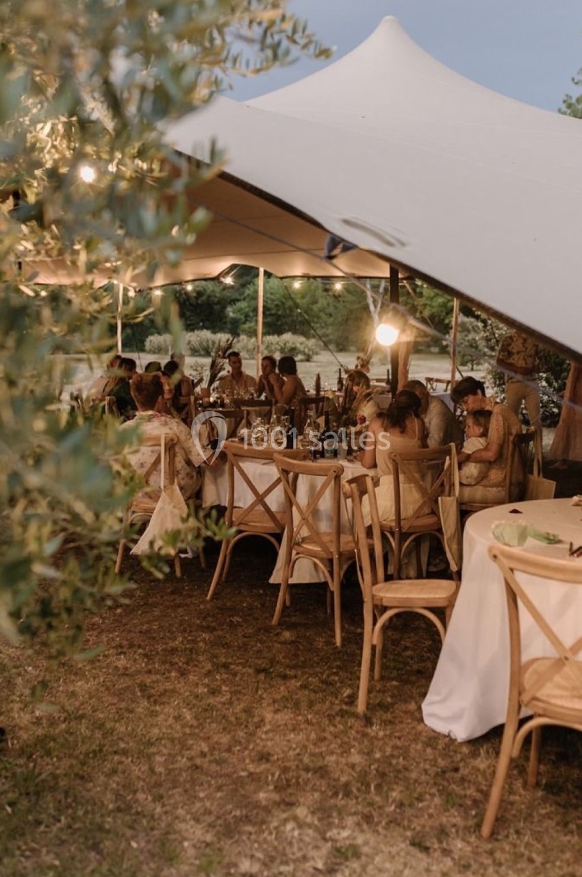 Des invités dînent sous une tente élégante, entourés de tables décorées et de végétation en plein air.