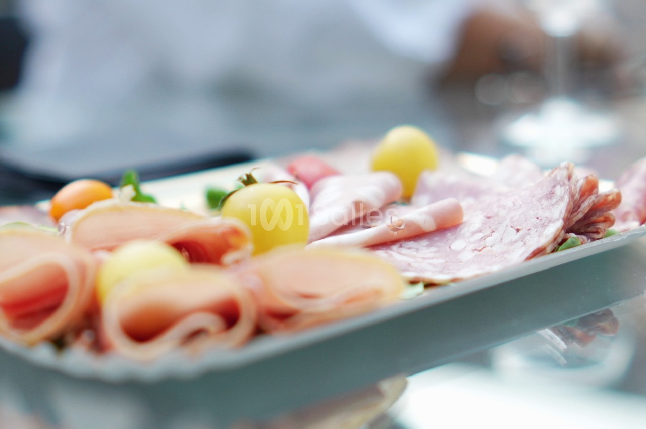 Plateau de charcuterie en tranches roulées et salami, accompagné de petites tomates cerises jaunes et orange et de feuilles de roquette.