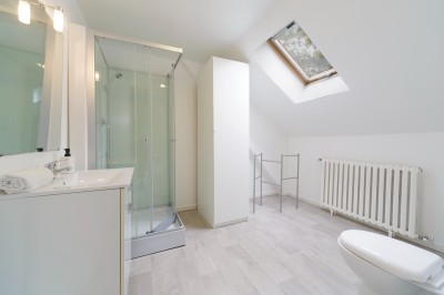 Salle de bain lumineuse avec lavabo, miroir, douche vitrée et sol en bois clair, vue sur un extérieur verdoyant.