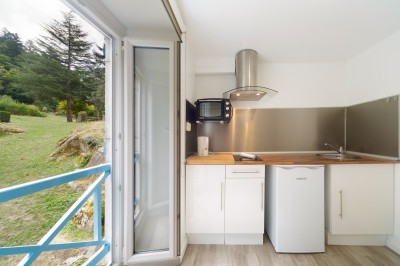 Salle de bain lumineuse avec lavabo, miroir, douche vitrée et sol en bois clair, vue sur un extérieur verdoyant.