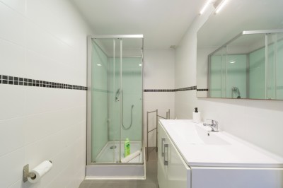 Salle de bain lumineuse avec lavabo, miroir, douche vitrée et sol en bois clair, vue sur un extérieur verdoyant.