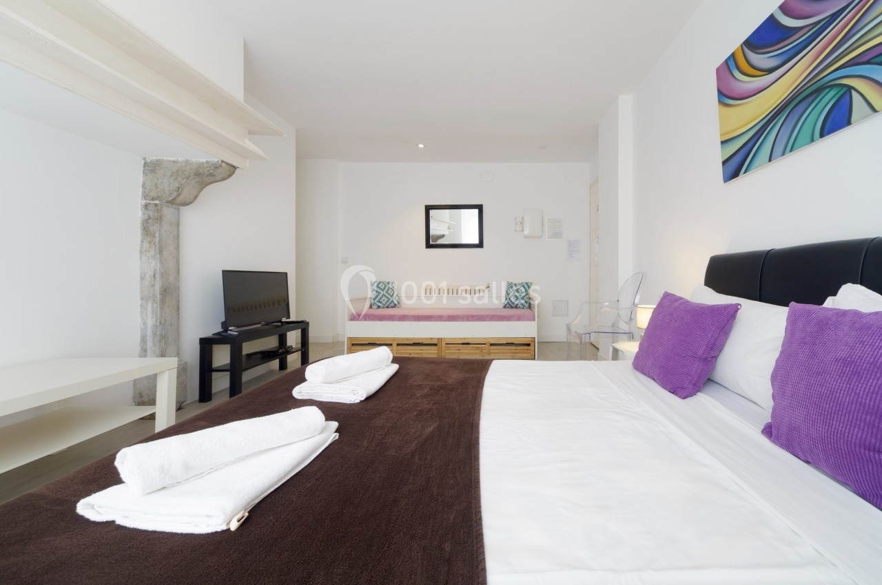 Chambre lumineuse avec lit double, canapé-lit, télévision, décor moderne et linge de lit plié sur le lit.