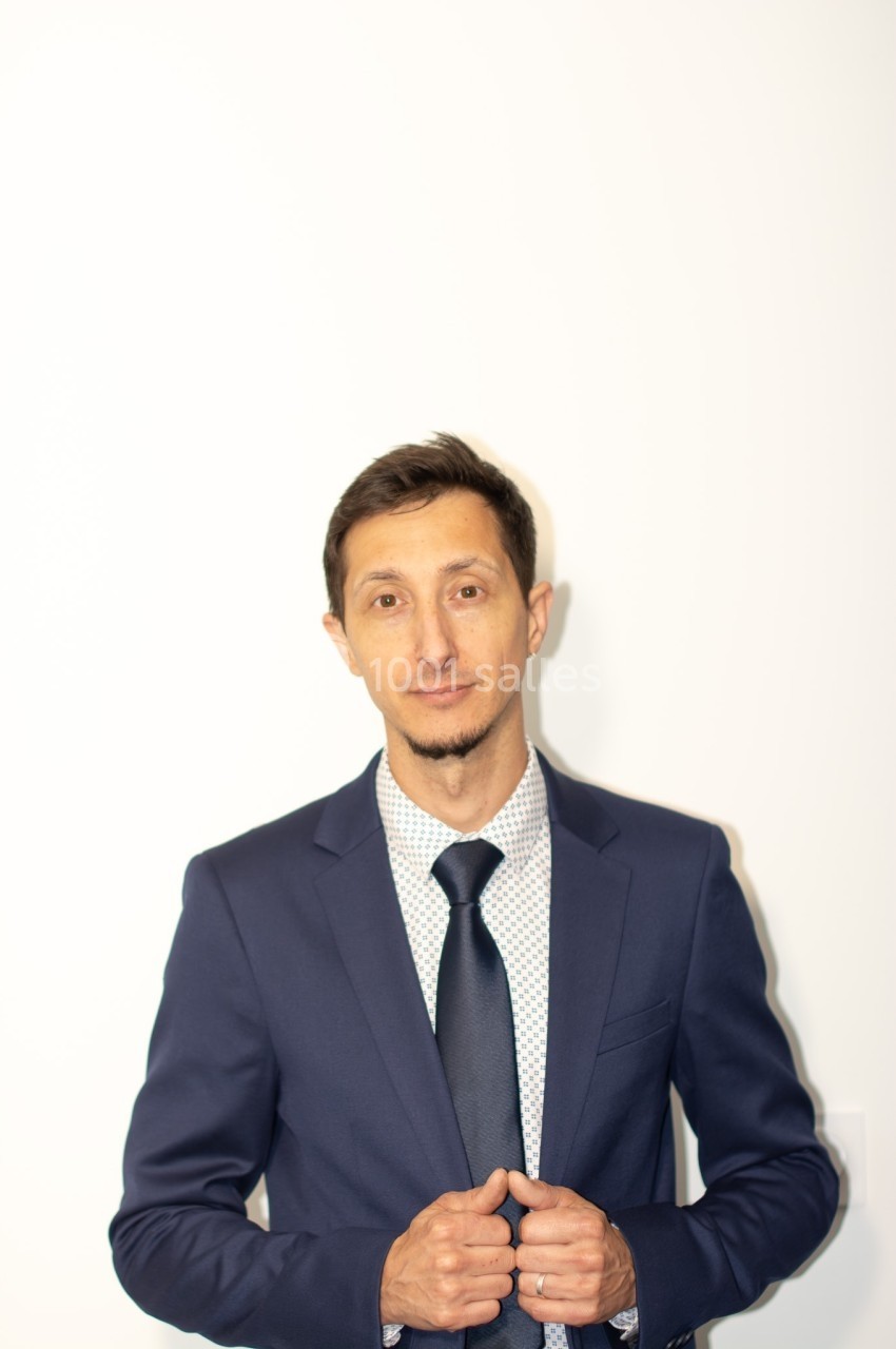 Homme en costume bleu ajustant sa veste devant un fond blanc.