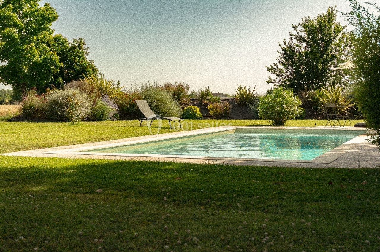 Piscine extérieure entourée de pelouse, de chaises longues et de végétation sous un ciel dégagé.