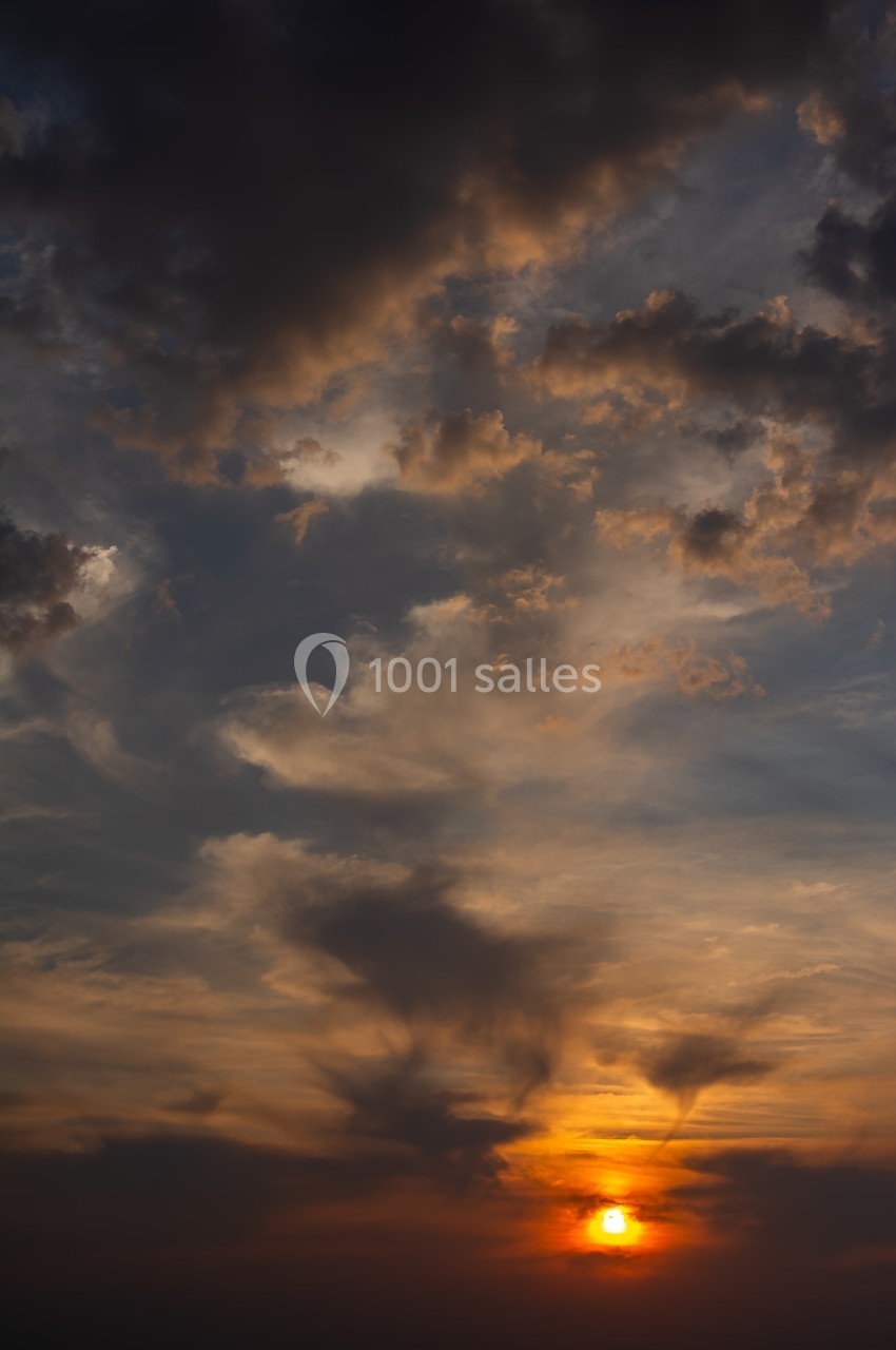 Ciel au coucher du soleil avec des nuages sombres et des teintes orangées illuminant l'horizon.