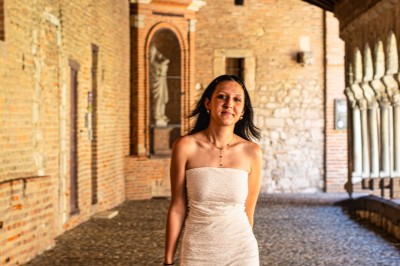 Miniature Event Shoot #8 Une femme en robe blanche marche dans une galerie couverte en pierre avec des arches et des murs en briques.