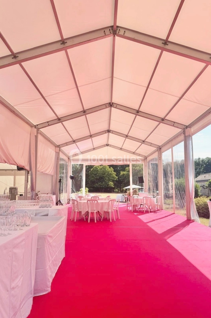 Intérieur d'une tente événementielle avec sol rouge, tables dressées et vue sur un jardin en arrière-plan.