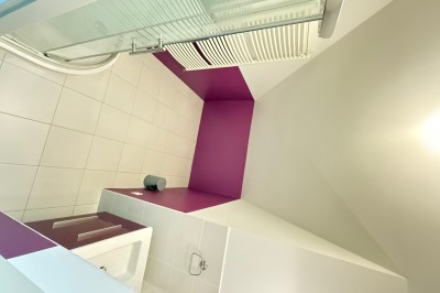 Intérieur d'une tente événementielle avec sol rose, tables blanches et vue sur un espace extérieur verdoyant.