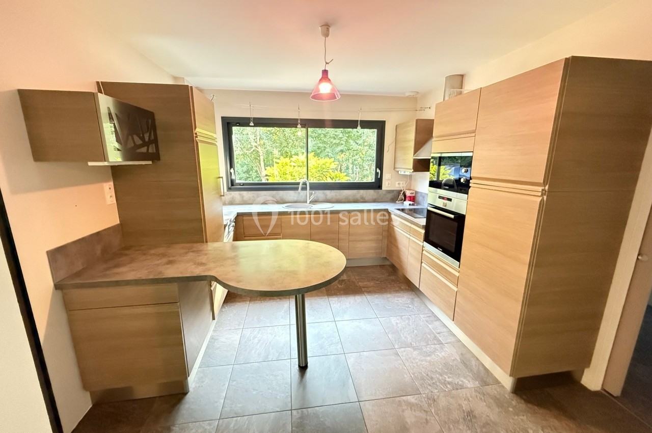 Cuisine moderne avec meubles en bois clair, plan de travail en pierre, table intégrée et grande fenêtre donnant sur un…