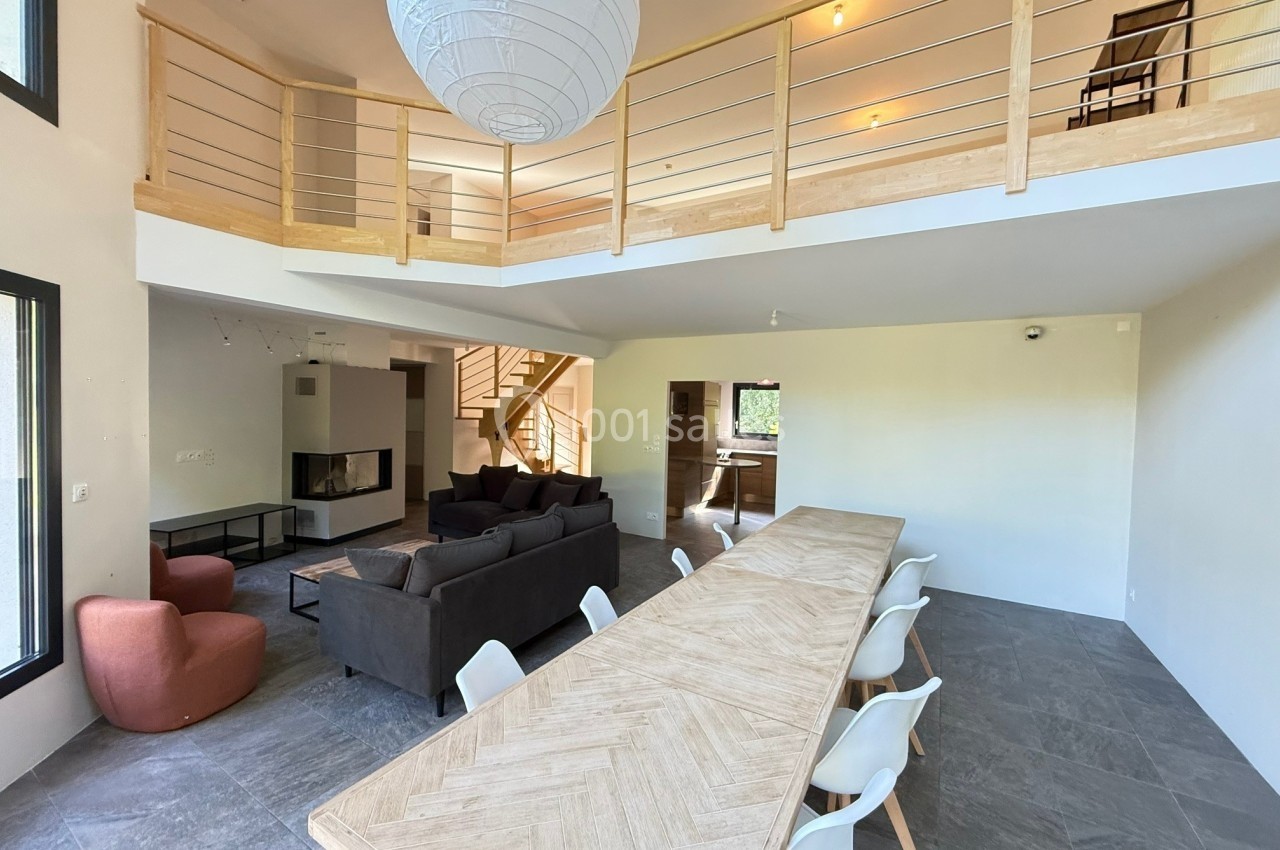 Salle à manger spacieuse avec une grande table en bois, salon avec canapés et mezzanine en arrière-plan.