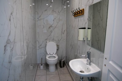 Salle de bain moderne avec murs en marbre, toilettes, lavabo, miroir et porte-manteaux en bois.