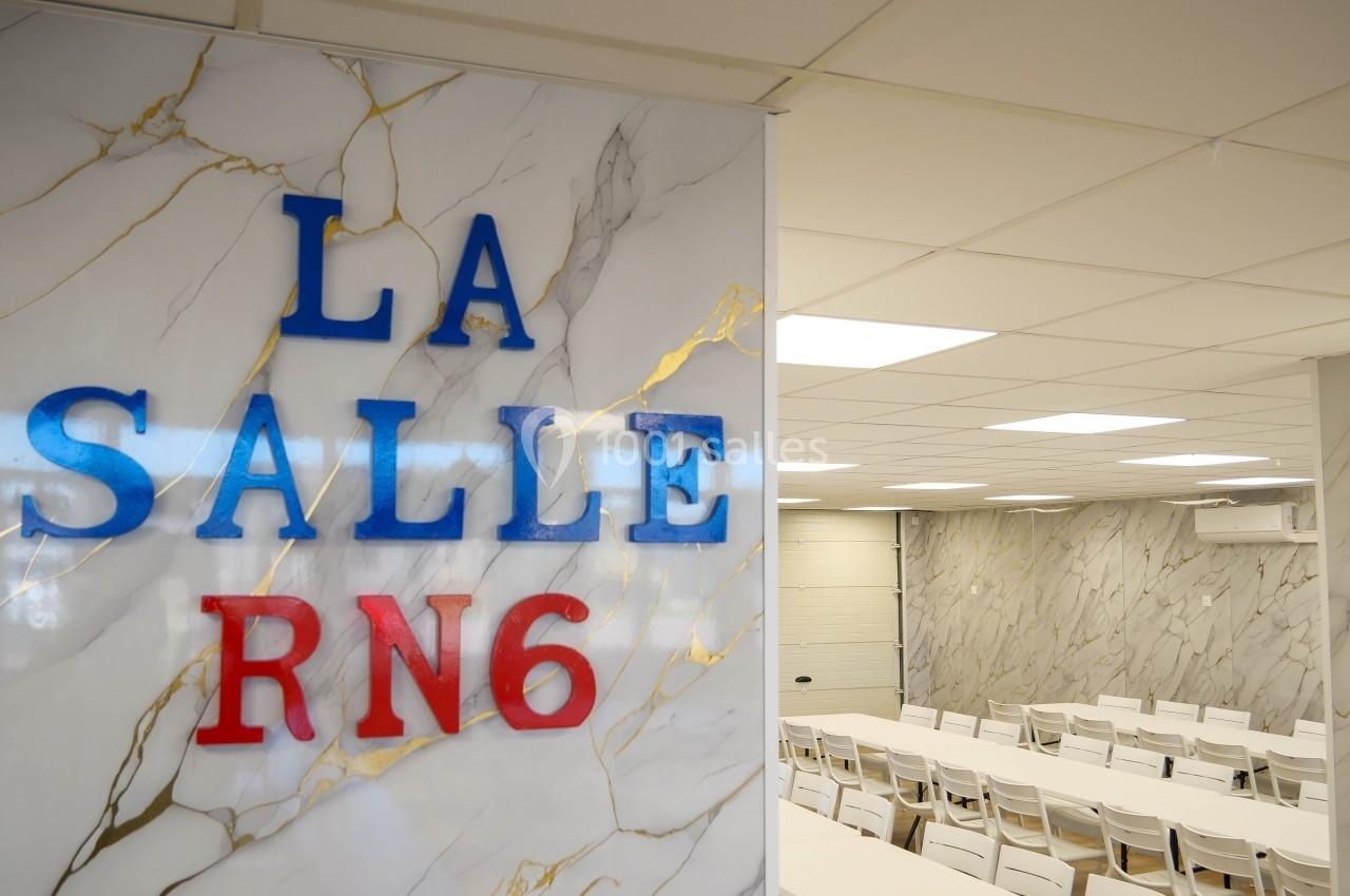 Mur avec l'inscription ’La Salle RN6’ et vue sur une salle de réunion équipée de tables et chaises blanches.