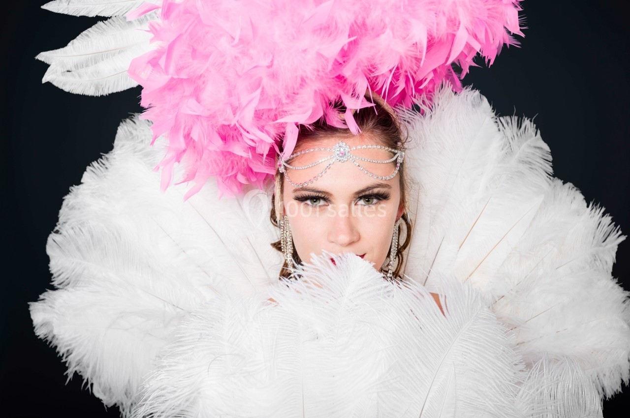 Femme portant une coiffe rose avec des plumes blanches, regardant directement l'objectif.