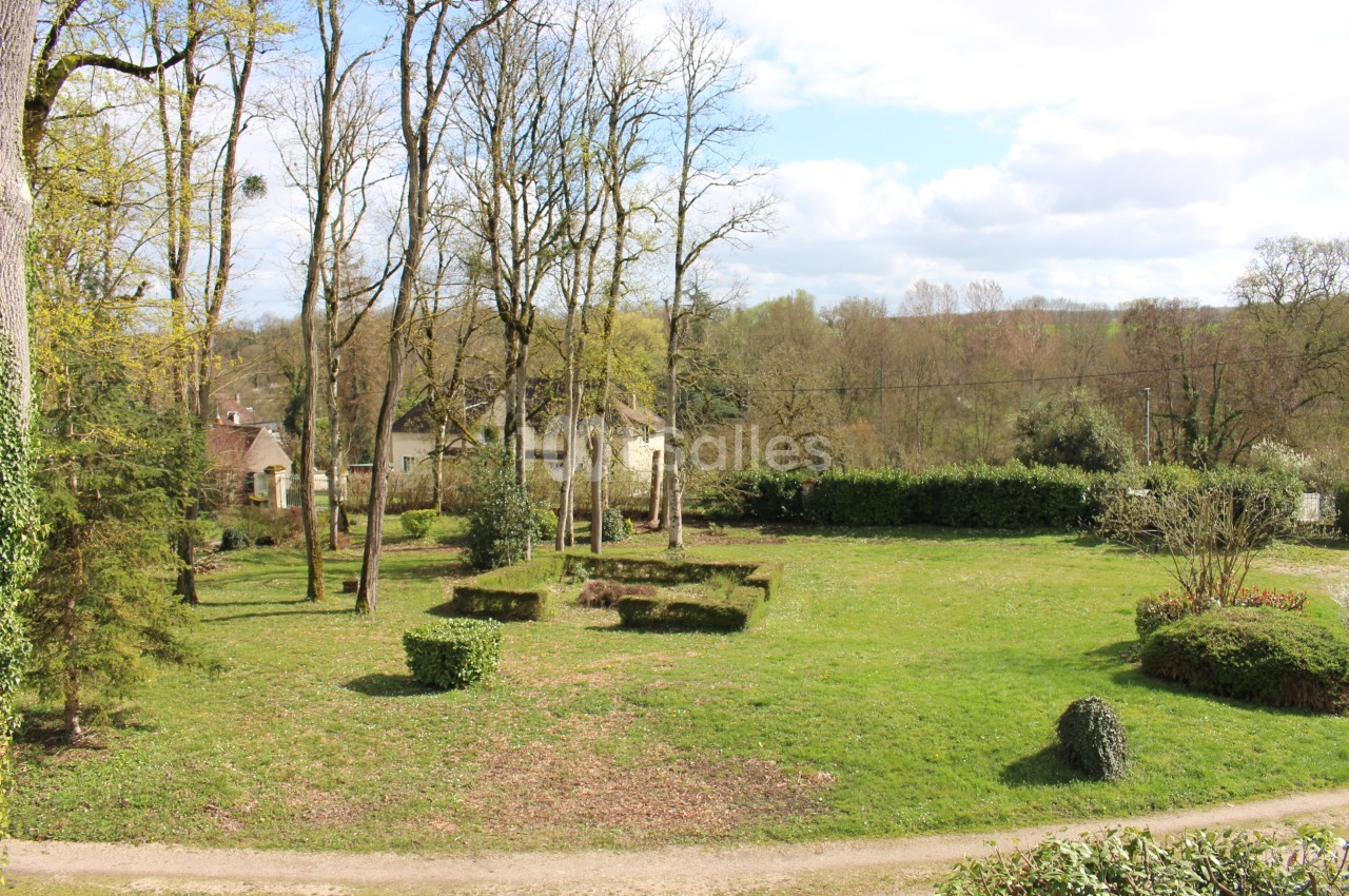 Vue extérieure d'une pelouse entourée d'arbres dépouillés, avec des buis taillés en formes géométriques et quelques maisons en arrière-plan. Wait, I must not start with "Vue de" - the rule says never start with "Photo de", "Image de", "Vue de". My draft