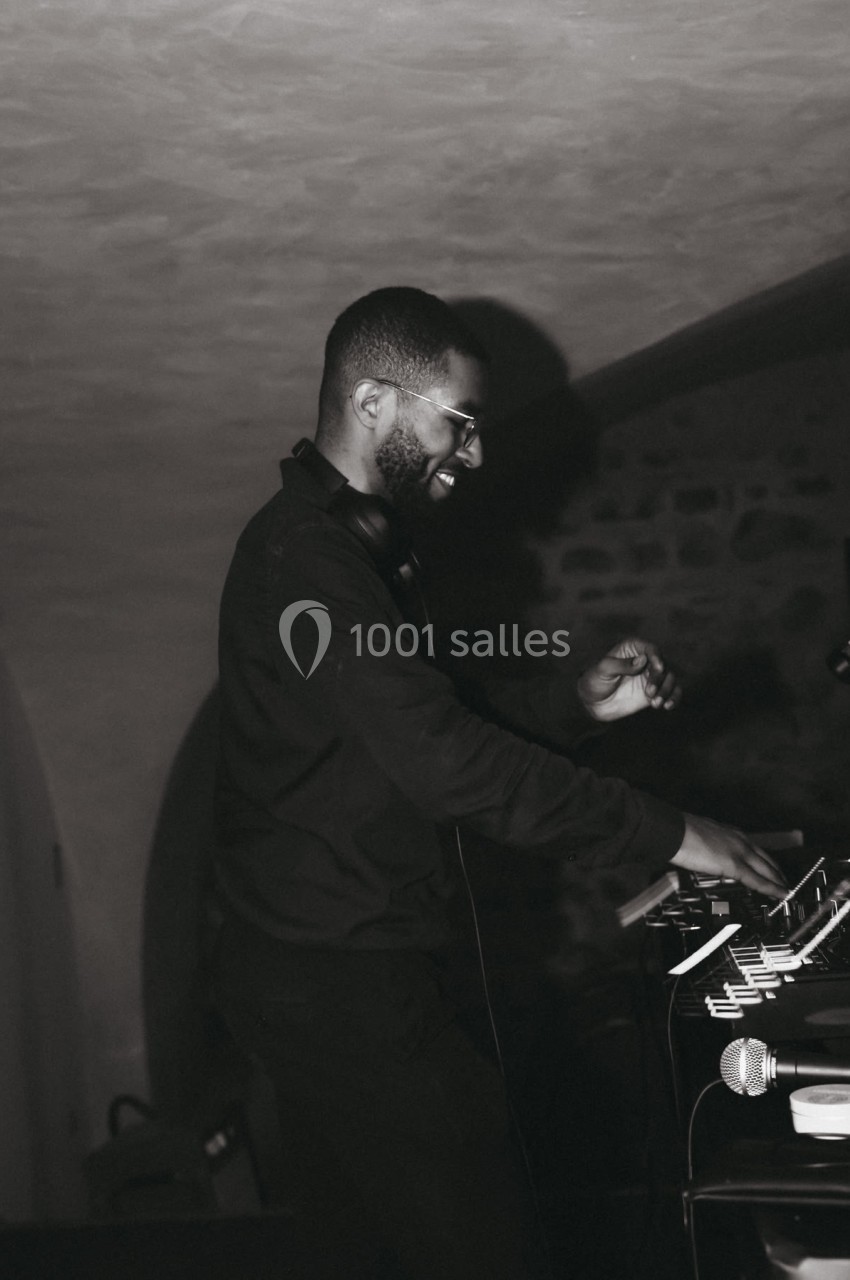 Un DJ mixant de la musique dans un espace intérieur sombre avec des murs en pierre.