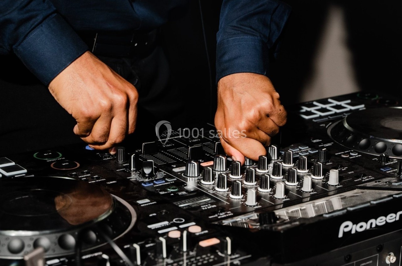 Mains ajustant les commandes d'une table de mixage audio dans un environnement sombre.